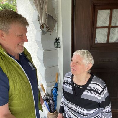 Mann steht lachend mit älterer Frau an deren Haustür.