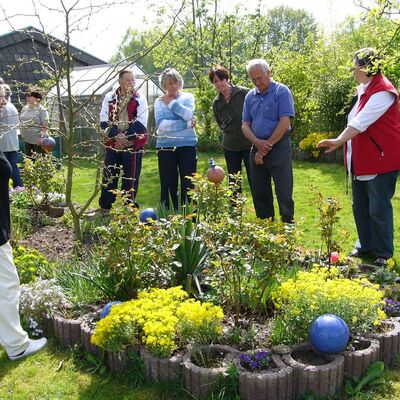 Bild mit fünf Frauen und Männern, die um ein schön gestaltetes Blumenbeet in einem Garten stehen, ein Mann erklärt etwas dazu.