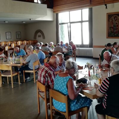 Vorwiegend ältere Männer und Frauen sitzen in Gruppen an Tischen und essen.
