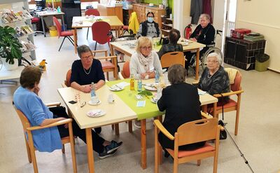 Acht Personen sitzen an zwei Gruppentischen mit Kaffee und Kuchen.