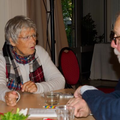 ältere Frau und älterer Mann sitzen gemeinsam an einem Tisch und reden miteinander