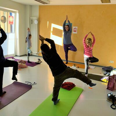 Yogalehrerin zeigt einbeinigige Übung vor vier Kindern in gleicher Pose