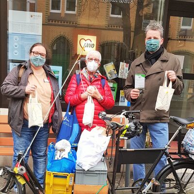 3 Personen mit Mundschutz stehen hinter voll gepacktem Lastenrad und halten Adventstütchen in der Hand.