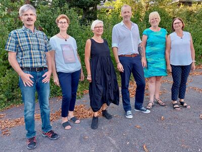 Vier Frauen und zwei Männer stehen in sommerlicher Kleidung nebeneinander vor Sträuchern