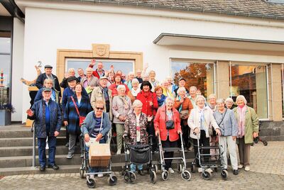 Gruppenfoto von gut gelaunten älteren Männern und Frauen auf einer Treppe stehend, die zum Teil winken