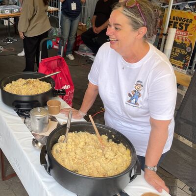 Frau steht an einem Stand mit zwei großen Behältern mit Essen zum Verkauf.