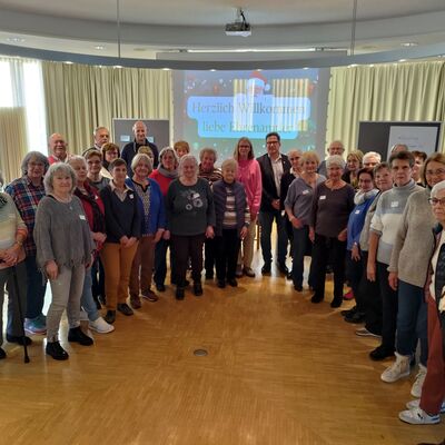 Gruppenbild mit vielen Männern und Frauen unterschiedlichen Alters, im Hintergrund eine Präsentation an der Wand.