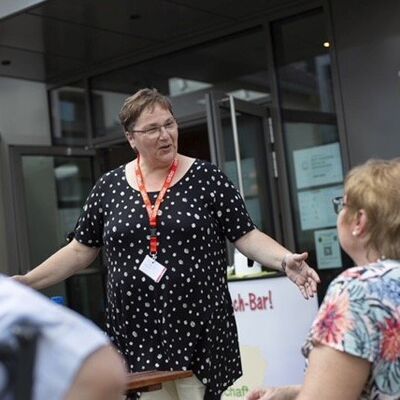 Frau Witsch unterhält sich mit ausgebreiteten Armene mit einer älteren Frau, die vor ihr sitzt