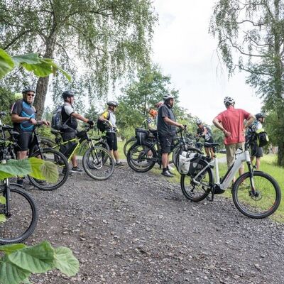 Bild mit ca. 12 Personen, die mit Fahrradhelmen und Rädern in der Natur stehen.
