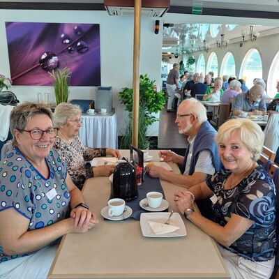 Bild mit älteren Frauen und Männern, die mit Kaffee an mehreren Tischen auf einem Ausflugsschiff sitzen.