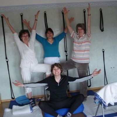 Gruppenbild vom vier Frauen, die Yogapositionen einnehmen. Rundherum Yoga-Equipment.