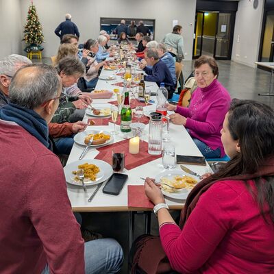 An einer großen Tafel mit Speisen udn Getränken sitzen Menschen unterschiedlichen Alters und Geschlechts.