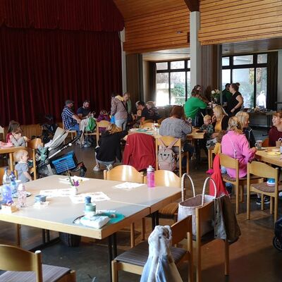 In einem Pfarrsaal sitzen Menschen allen Alters an Tischen zusammen, unterhalten sich und lachen
