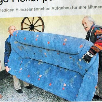 Zwei ältere Männer tragen ein blaues Sofa einer älteren Frau.