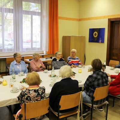 Ältere Personen am Tisch hören Gedächtnistrainer am Tischende zu.