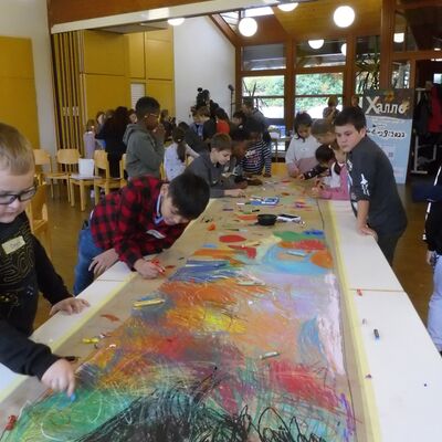 Kidner stehen an langem Tisch und malen mit bunter Farbe