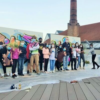 Jugendliche und Betreuer mit Masken vor Wand mit bunten Graffiti