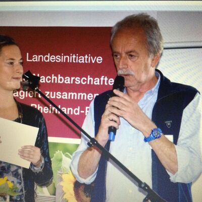 Frau und Mann mit Mikrofon vor einem Aufsteller der Landesinitiative