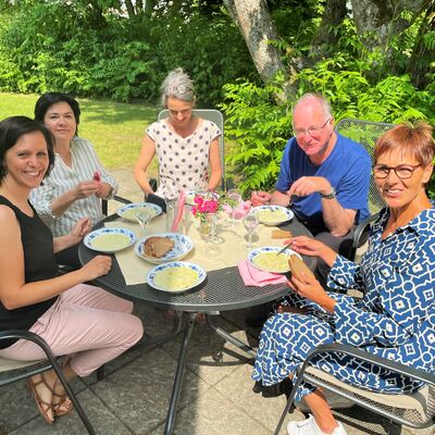 Drei Frauen und ein Mann sitzen am Tisch im Freien und essen Suppe