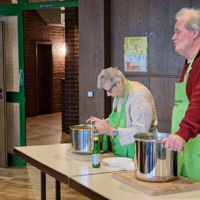 Bild mit Mann und Frau ein einem Tisch mit großen Suppentöpfen vor ihnen.