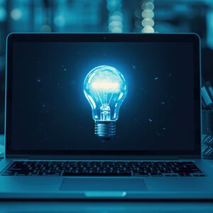 Bild von einem augeklappten Laptop auf Tisch, auf dem Bilschirm leuchtet eine Glübirne