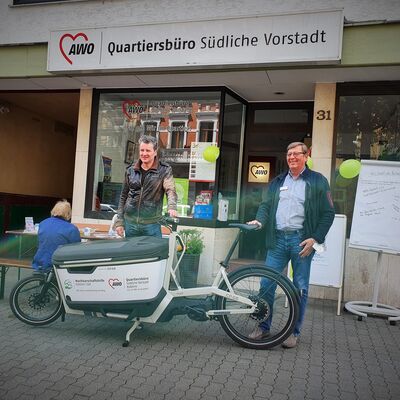 2 Männer stehen hinter elektrischem Lastenrad auf der Straße vor dem Quartiersbüro
