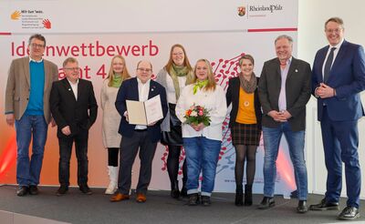 Gruppenfoto mit Menschen auf einer Tribüne, eine Person hält eine Preisurkunde in der Hand