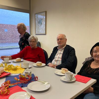 Zwei Frauen eine mit Kopfbedeckung sitzen zusammen an einem Tisch, darauf Kaffee, Fassnachtsgebäck und Luftschlangen