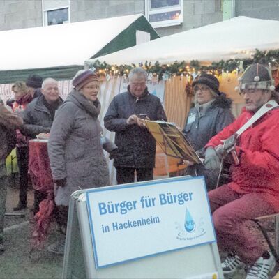 Gitarrenspieler und Sängerin vor einem Weihnachtsnachtmarktstand, drum herum Besucher
