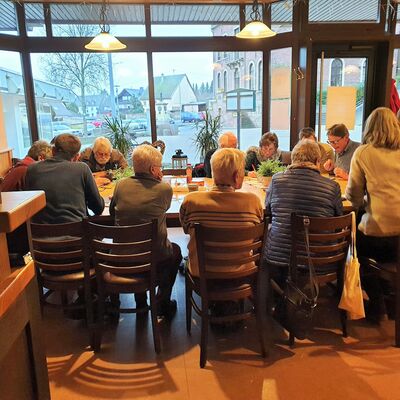 Viele ältere Frauen und Männer sitzen an großem Gruppentisch.