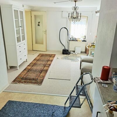 Blick von der Küche ins Wohnzimmer mit Teppichen, Möbeln aber auch Werkzeugen