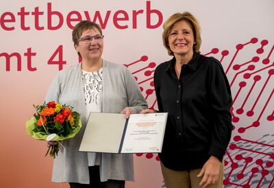 Die Ministerpräsidentin überreicht Urkunde und Blumenstrauß an eine Frau der Caritas