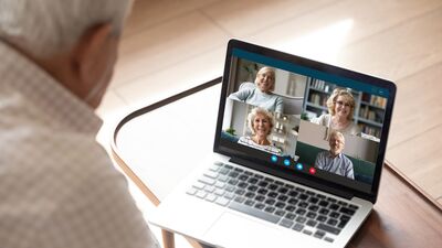 Älterer Mann sitzt vor Laptop, auf dem Bildschirm weitere vier Teilnehmende einer Videokonfernenz