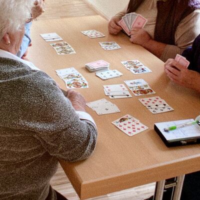 Drei Damen sitzen am Tisch auf dem aufgedeckte Spielkarten liegen