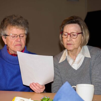 Zwei ältere Frauen lesen gemeinsam in einm Text an einer Kaffeetafel
