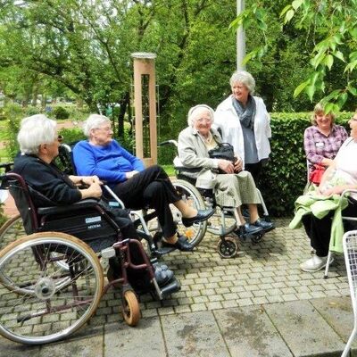 Zusammensitzen einer Gruppe von Menschen, zum Teil in Rollstühlen, auf einer Terasse