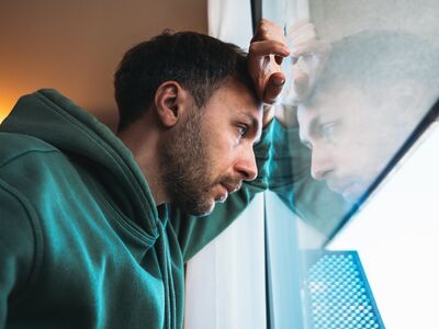 Bild mti einem mittelalten Mann, der traurig schaut und der mit Hand und Kopf an einem Fenster lehnt
