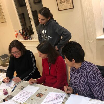 Eine Frau erklärt drei weiteren Frauen, wie man kalligraphisch schreibt