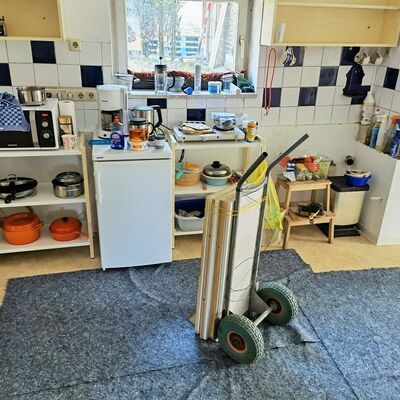 Küche mit ersten Möbeln und Utensilien, Sackkarre mit Regalbrettern steht auf Bodenschutz