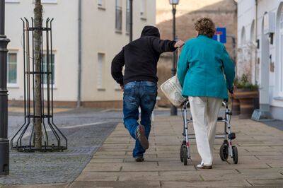 Frau mit Rollator und Handtasche, Vorbrennender Mann mit schwarzer Kapuze greift nach der Handtasche