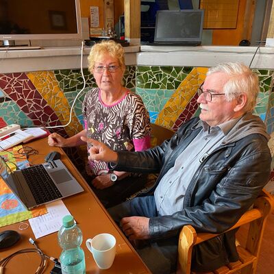 Älterer Mann und ältere Frau sitzen am Laptop vor Theke mit buntem Steinmosaik