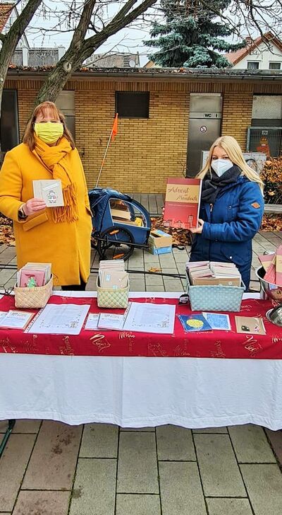Zwei Frauen mit Mundschutz stehen draußen an einem Bazartisch und verkaufen Weihnachtskarten
