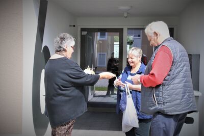 Frau überreicht Lesezeichen an Mann und Frau in der Nachbarschaft.