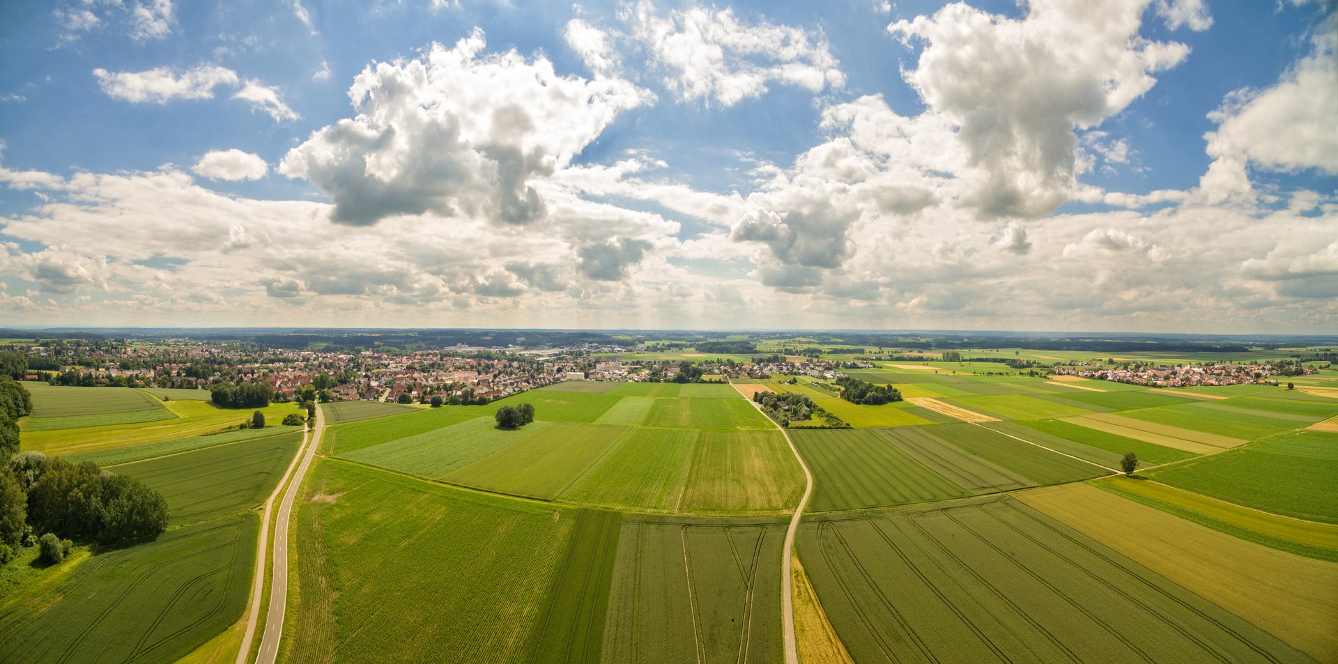 Luftbildaufnahem eines Dorfes umgeben von Wiesen und Wäldern, blauer Himmel mit weißen Wolken