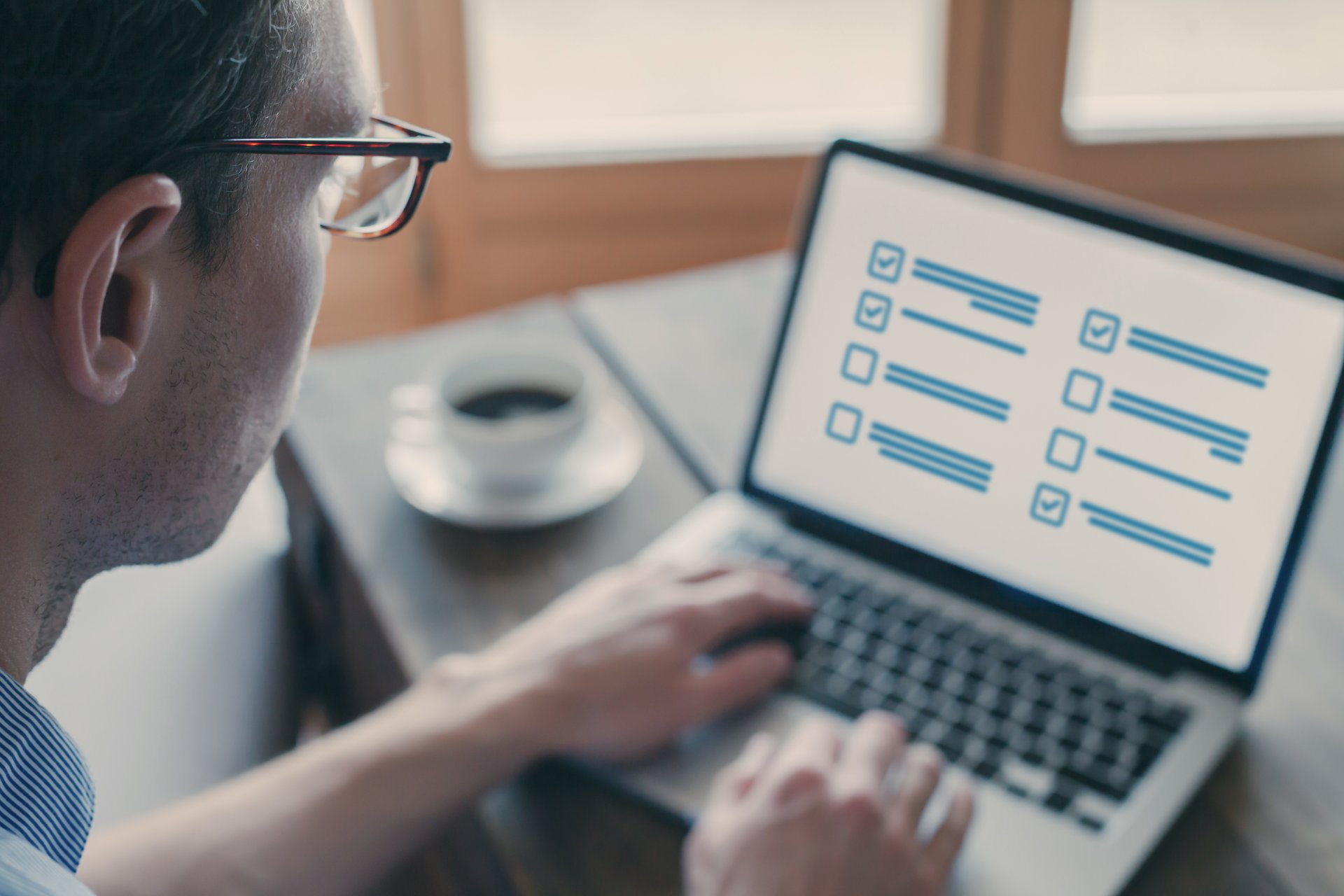 Mann mit Brille sitzt an einem Laptop auf dem Bildschirm sind Umfragekästchen zu sehen
