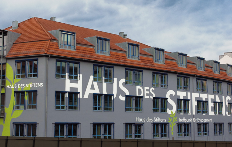Gebäudefassade mit vielen Fenstern, auf der mit Licht der Schriftzug Haus des Stiftens projiziert ist