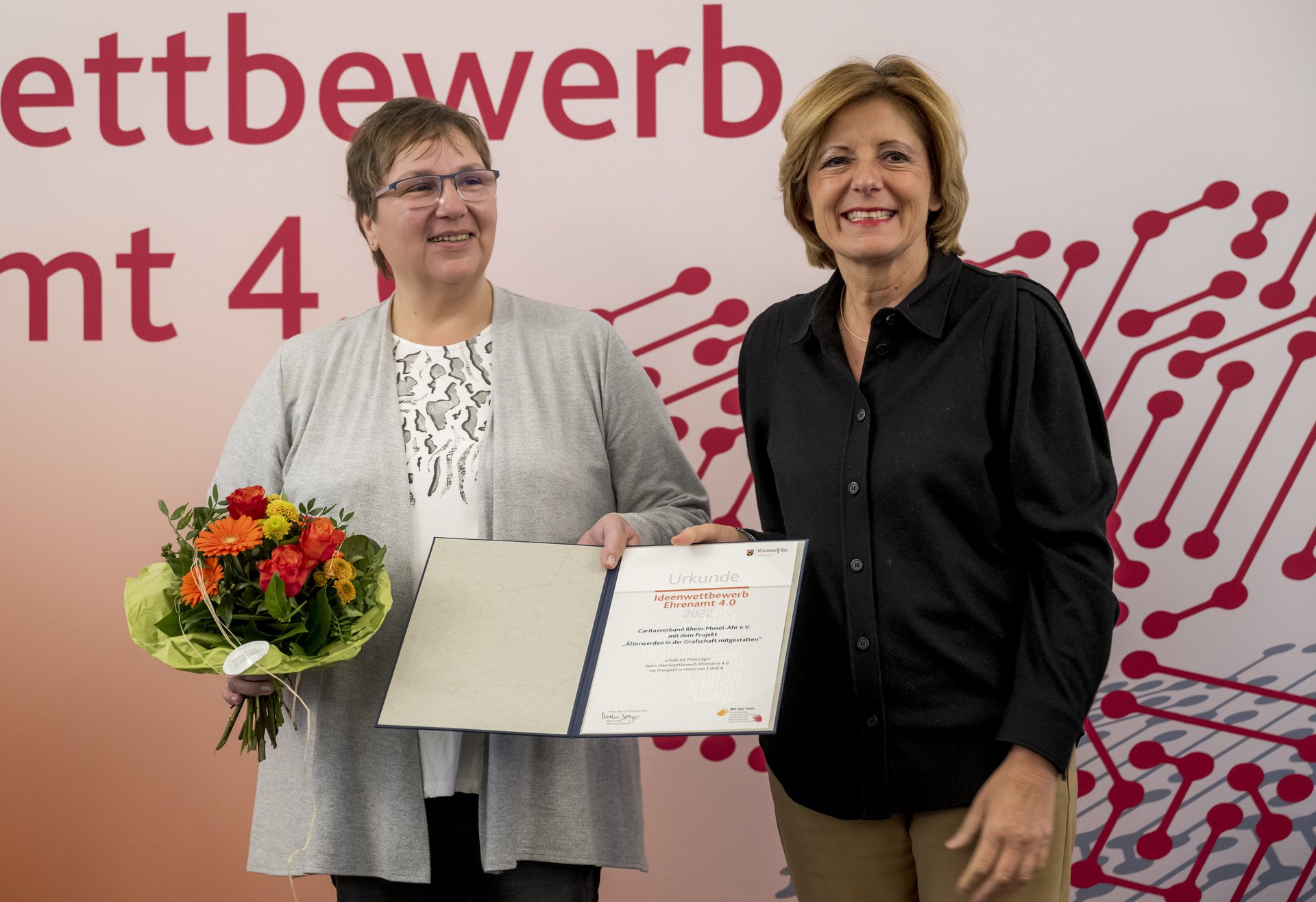 Die Ministerpräsidentin überreicht Urkunde und Blumenstrauß an eine Frau der Caritas