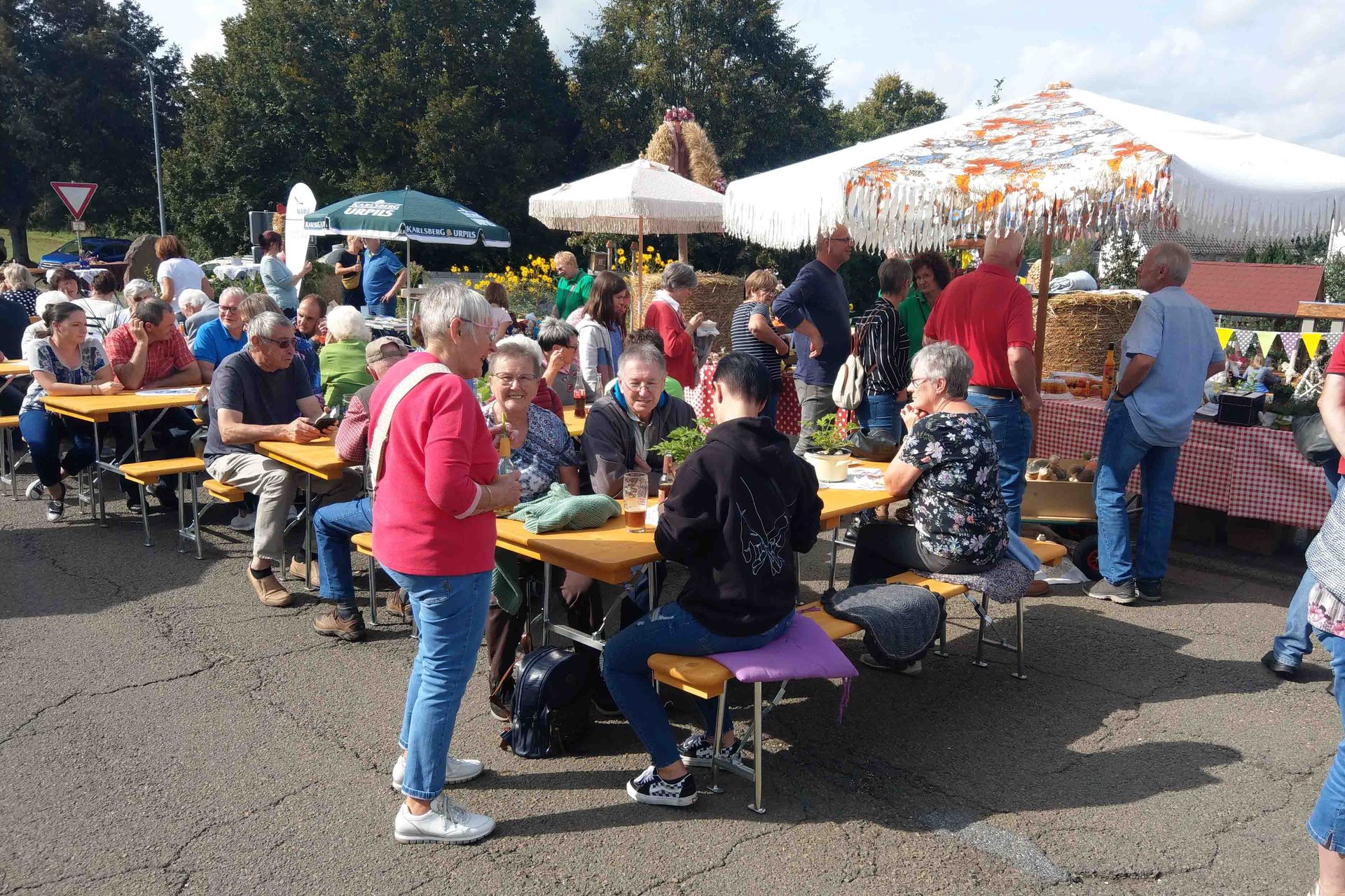 Menschen sitzen im Freien an Tischen auf Bänken in Gruppen, Sonneschirme