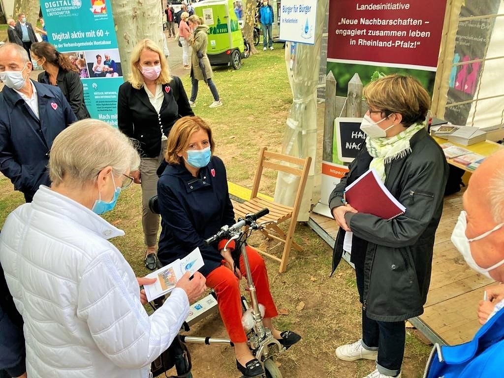 Malu Dreyer im Rollstuhl umgeben von Mitarbeitenden und Standbetreuer*innen