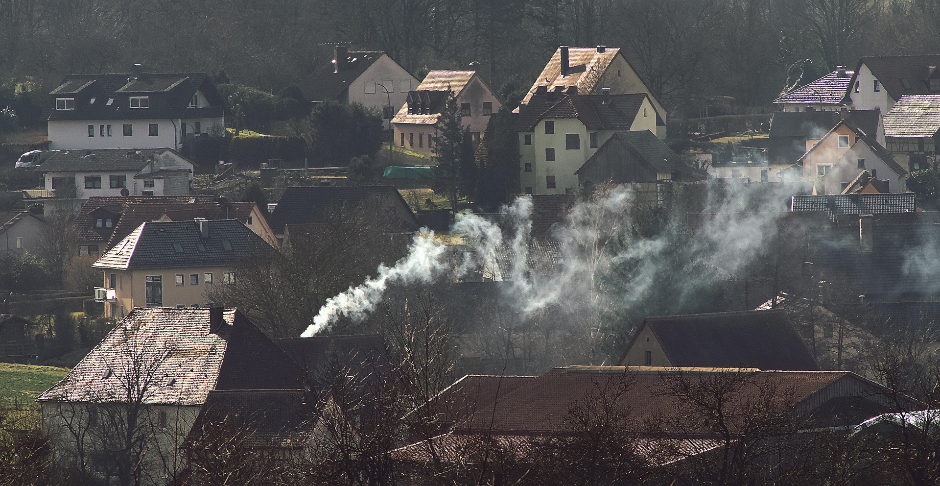 Bildausschnitt über eine Dachlandschaft eines kleinen Ortes auf dem Land, aus einem Schornstein steigt Rauch